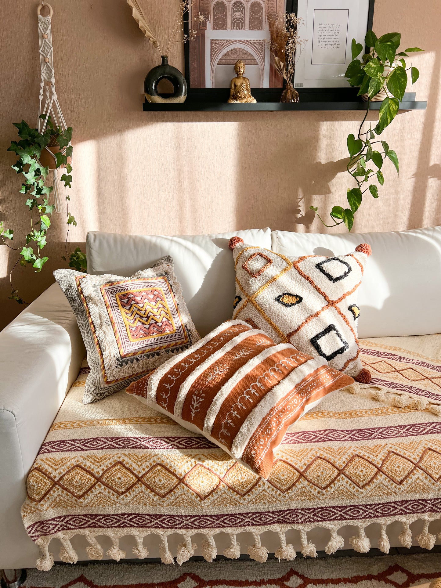 Bohemian living room setting featuring the ochre Nidhi cushion styled on a white sofa adorned with a tasseled throw and framed by climbing ivy.