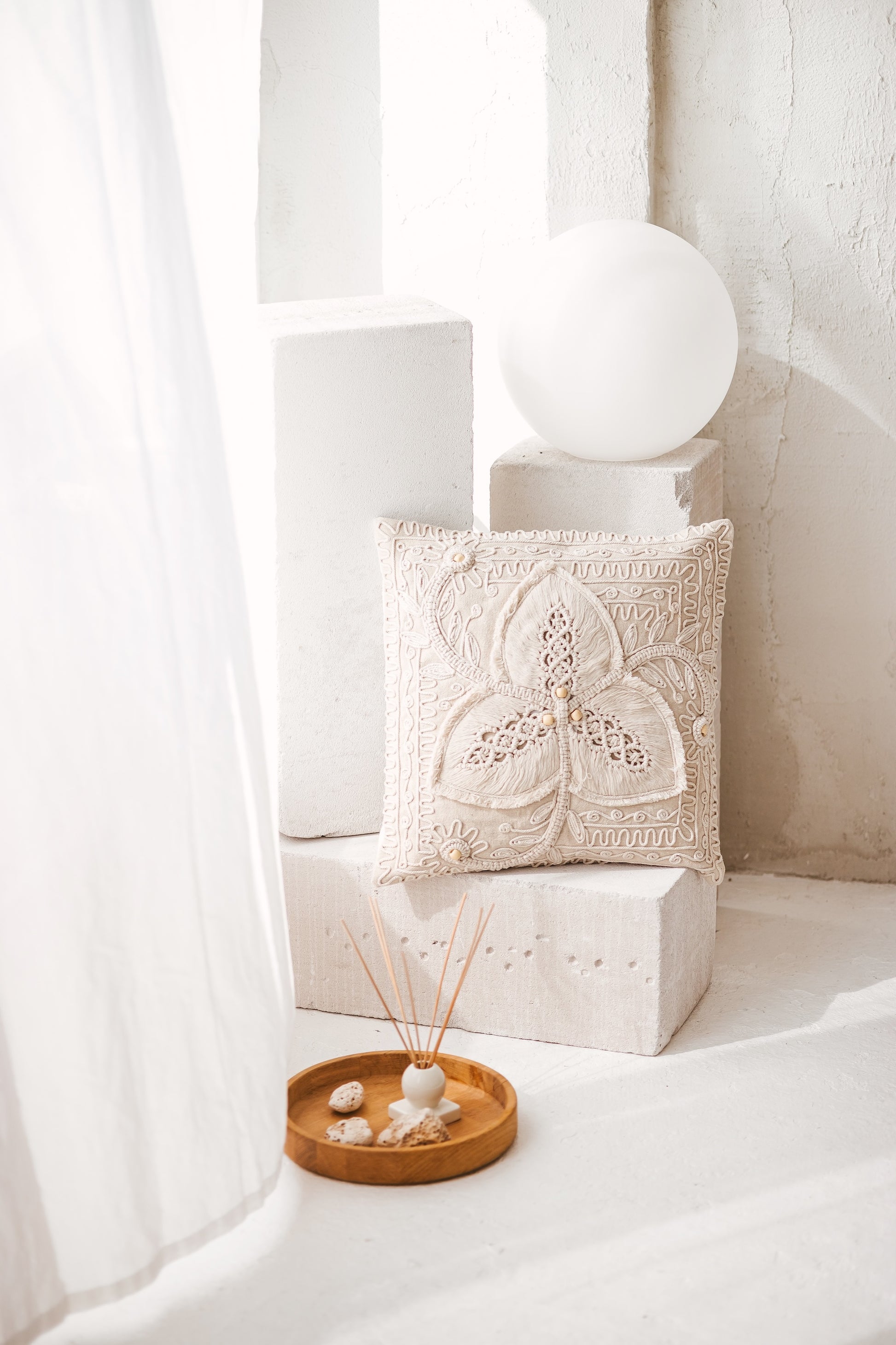 Handmade Svara macrame cushion cover featuring a natural cream cotton cord clover motif and wooden beads, styled in a bright minimalist interior.