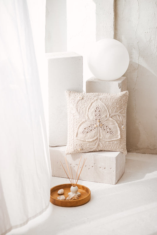 Handmade Svara macrame cushion cover featuring a natural cream cotton cord clover motif and wooden beads, styled in a bright minimalist interior.