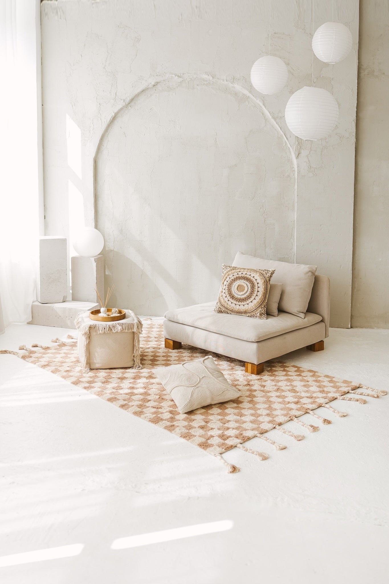 Frontal view of the square Saira cushion resting on an off-white sofa, clearly showing its centered, concentric mandala embroidery and jute details.