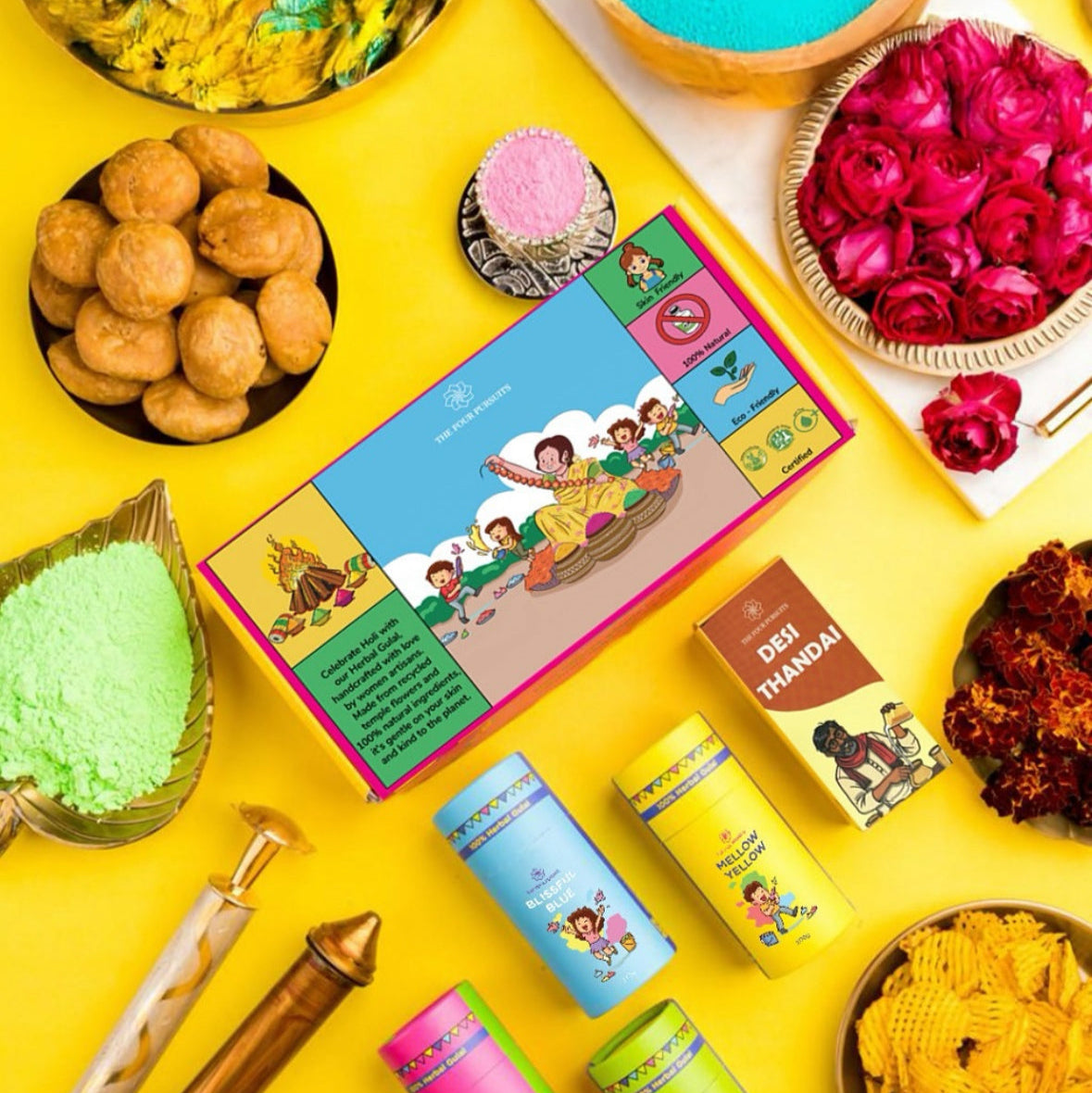 Complete Holi Gift Hamper flatlay featuring The Four Pursuits herbal gulal box, color canisters (Blue, Yellow, Pink ,Green), Thandai mix, and traditional sweets. The perfect premium Holi gift set.